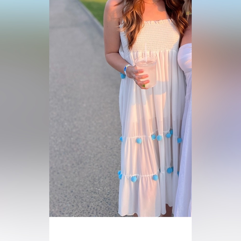 White smocked dress with tiered blue pom pom detail.